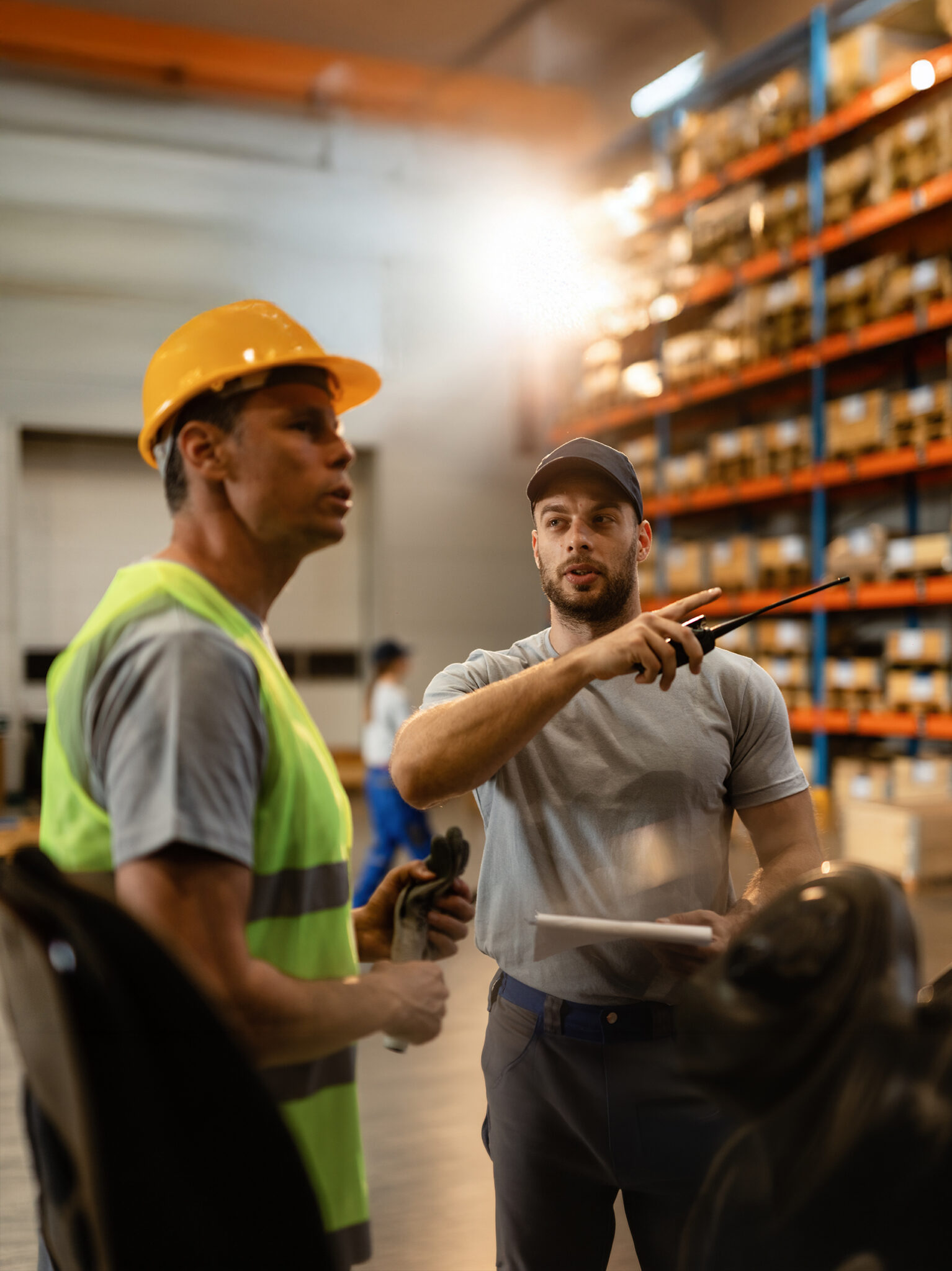 Warehouse dispatcher talking with a worker in industrial storage compartment.